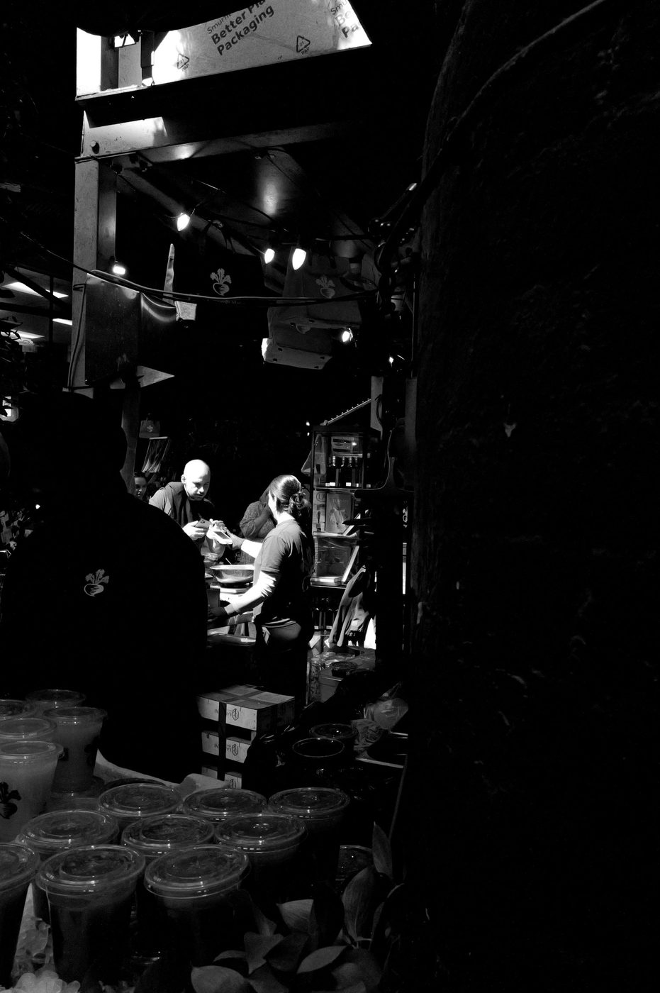 Vendor wrapping orders in the dim light of a covered market hall, London