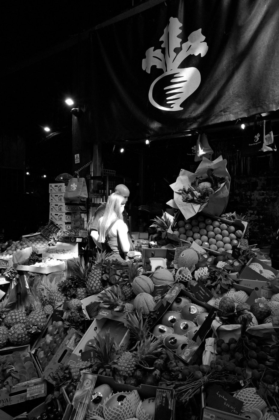 Customer choosing exotic fruit stacked under a stall's illustrated sign, London