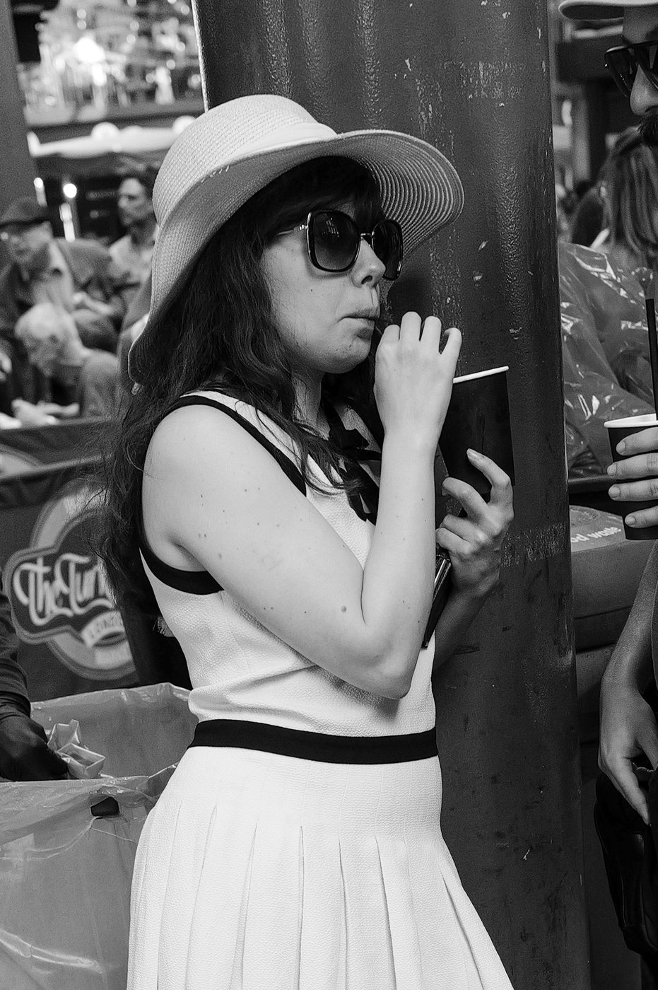 Woman in a straw hat and dark sunglasses sipping through a straw in the crowd, London