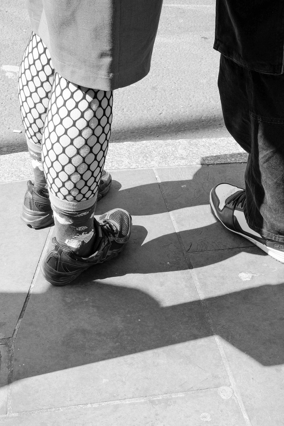 Close-up of legs in fishnet tights and sneakers, facing other shoes, London