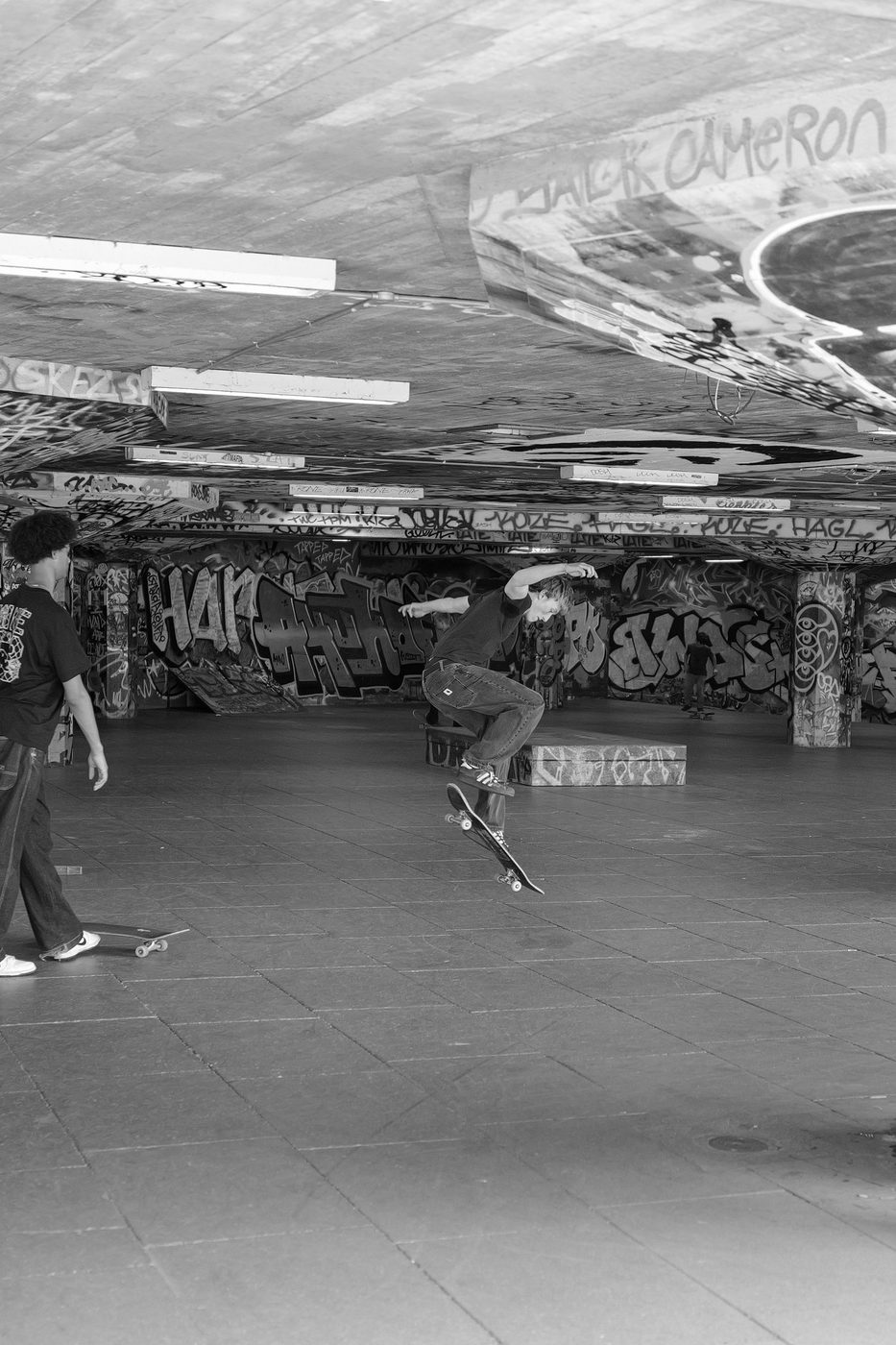 Skater mid-jump under the graffiti-covered arches of the Southbank skatepark, London