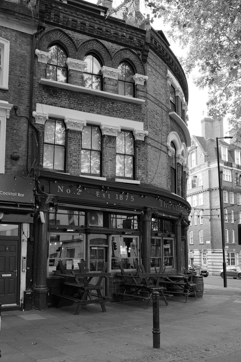 Curved facade of a historic corner pub founded in 1875, empty terrace in the early morning, London