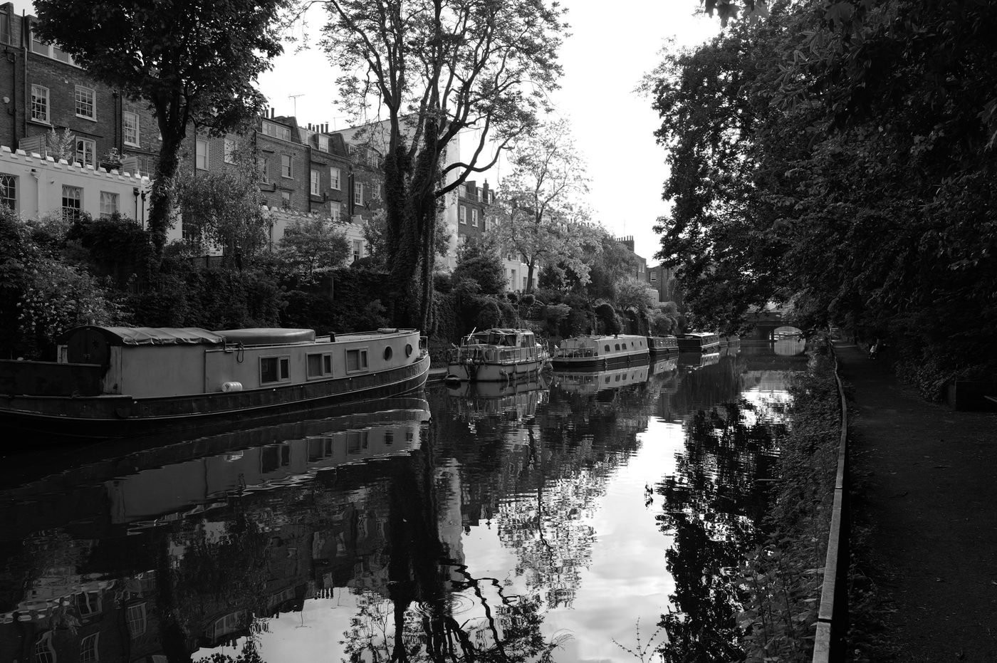 Narrowboats moored along the canal, brick houses reflected in the still water, London
