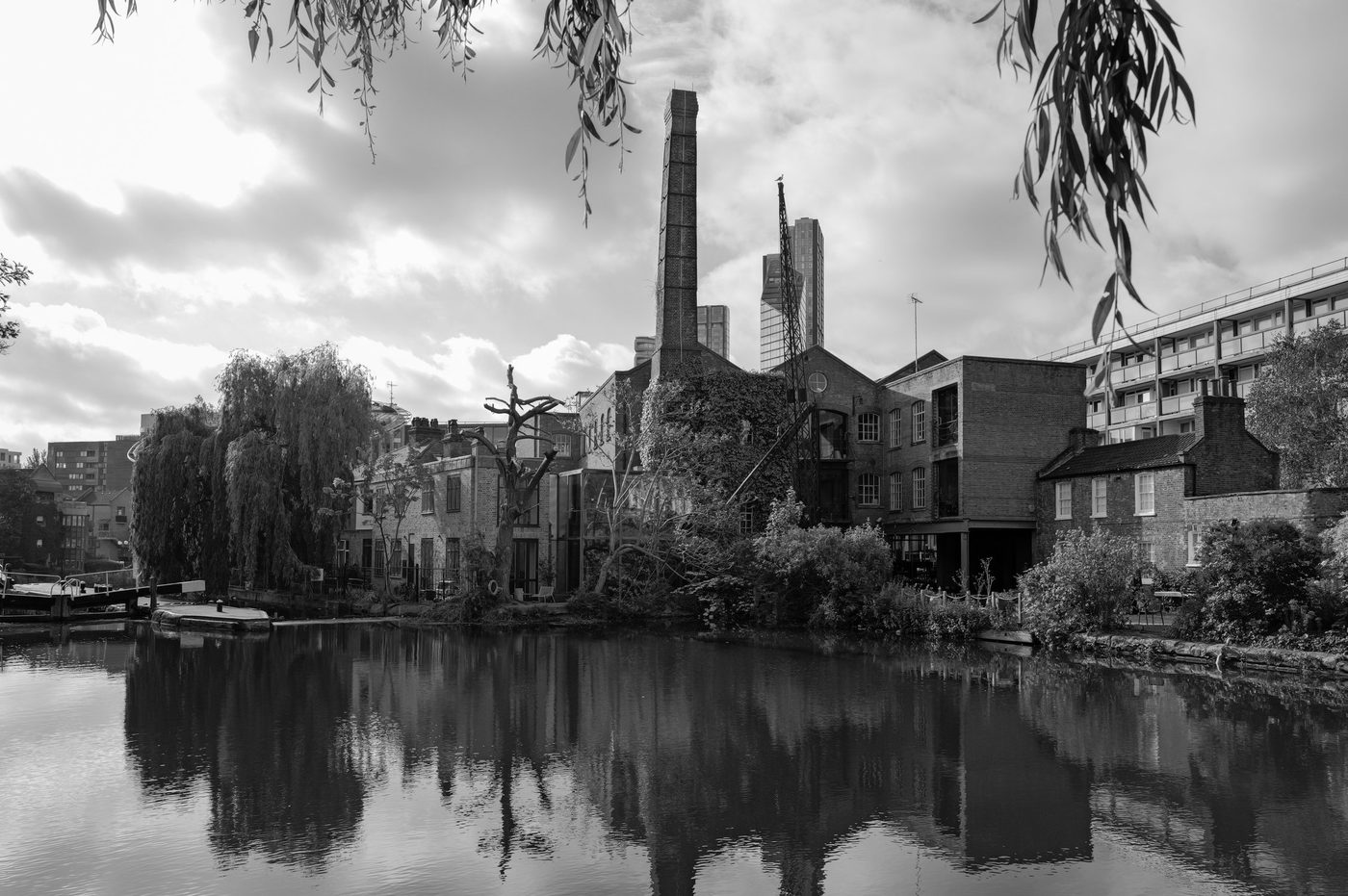 Old factory chimney between weeping willows and modern towers by the canal, London
