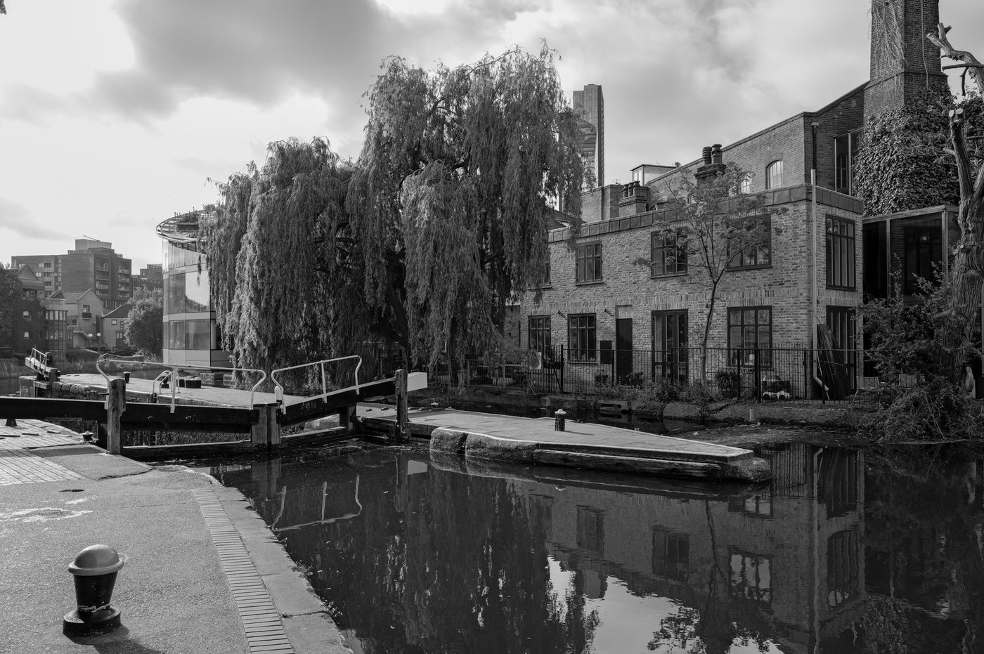 Canal lock lined with a weeping willow near converted old warehouses, London