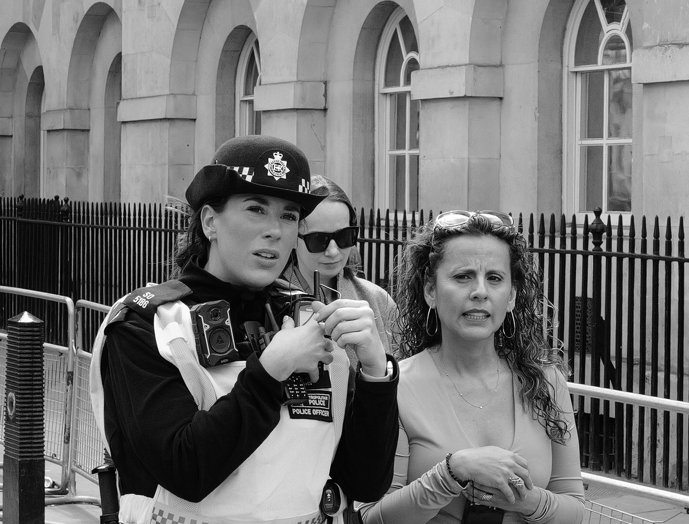Police officer in a high-visibility vest talking on the radio, surrounded by two passers-by, London