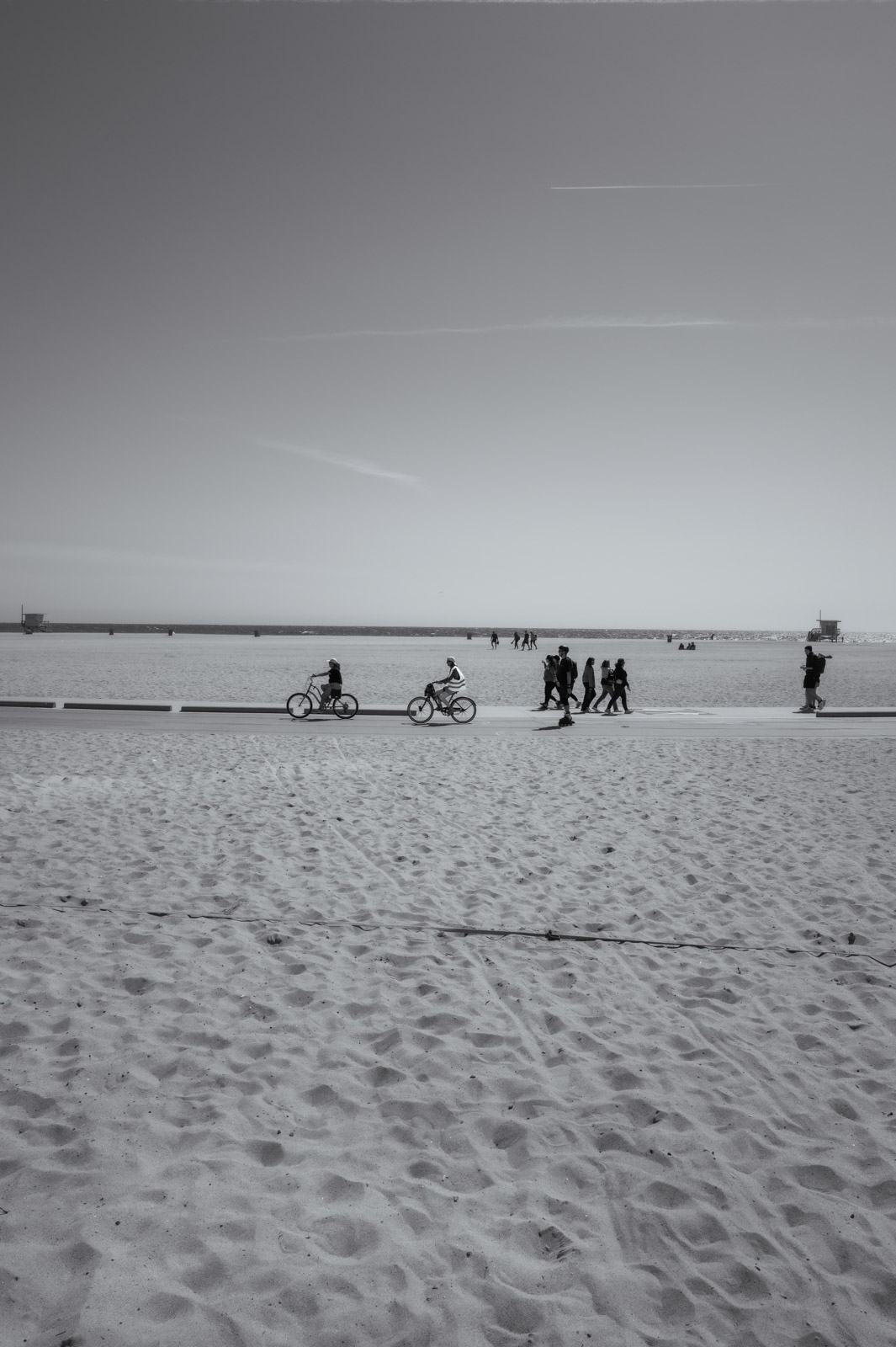 Cyclists and walkers crossing a wide beach, Los Angeles