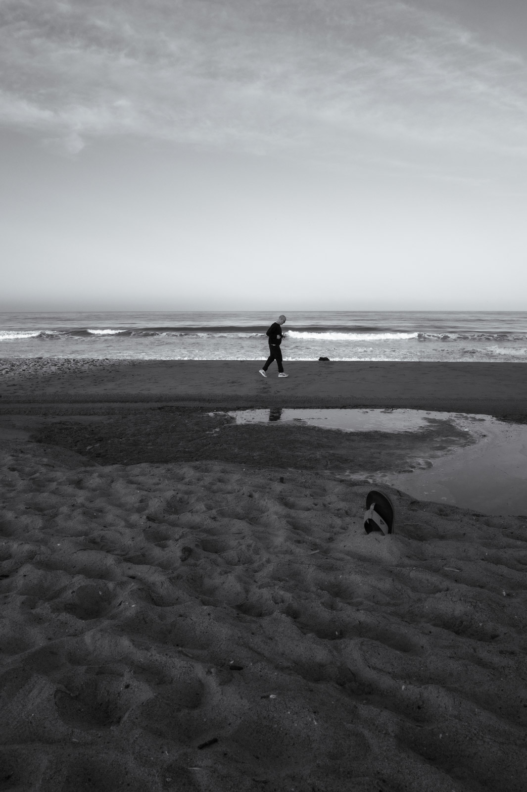 Lone walker passing a tide pool on the beach, Los Angeles