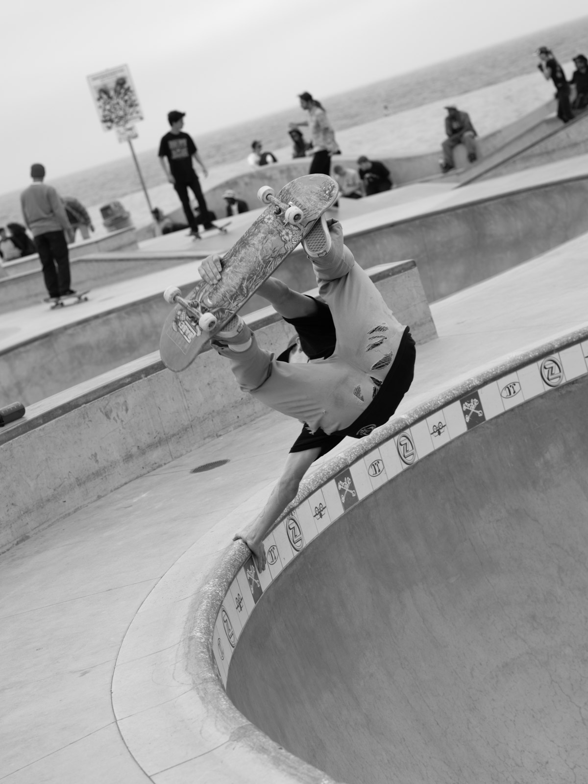 Skateboarder handstanding on the bowl's edge, onlookers around, Venice, Los Angeles