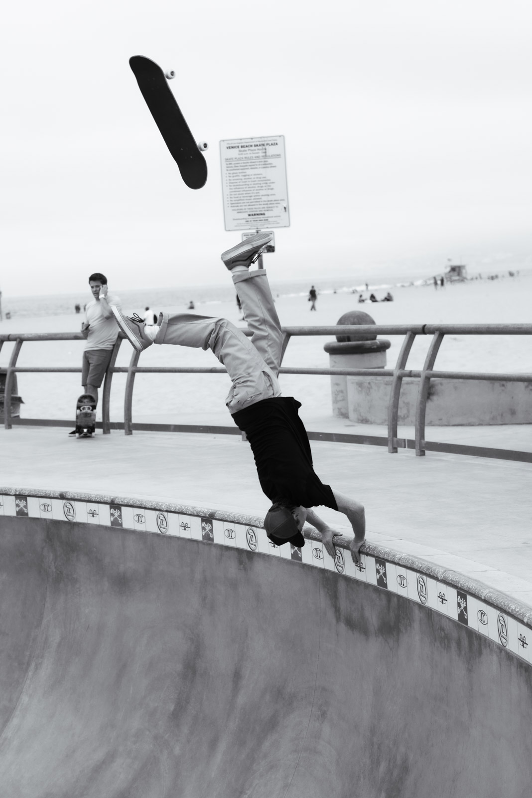 Skateboarder performing an inverted trick near a warning sign, Venice, Los Angeles