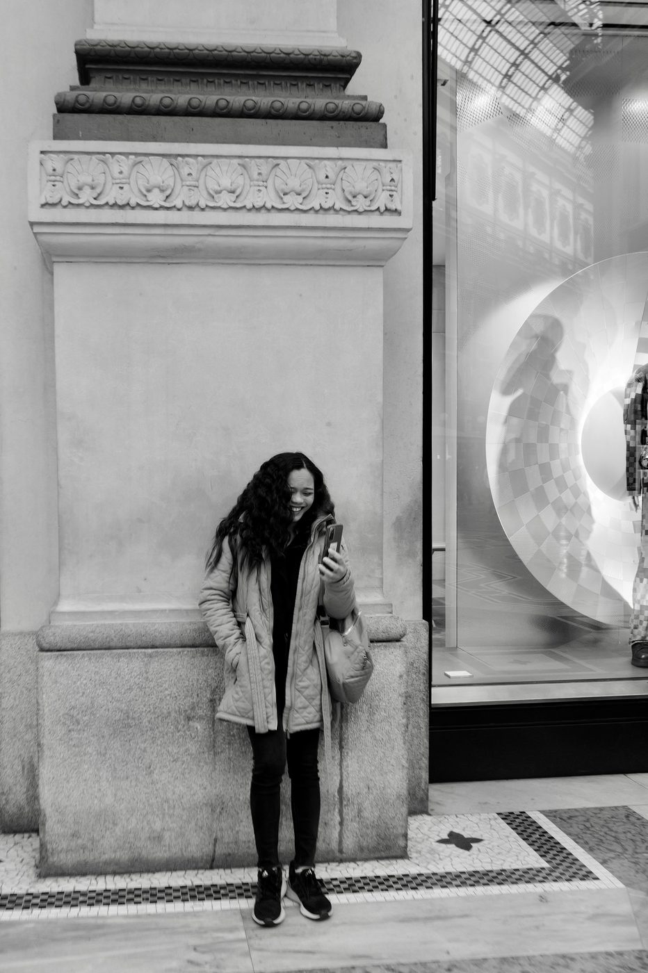 Young woman laughing at her phone, leaning against a carved column in the Galleria, Milan