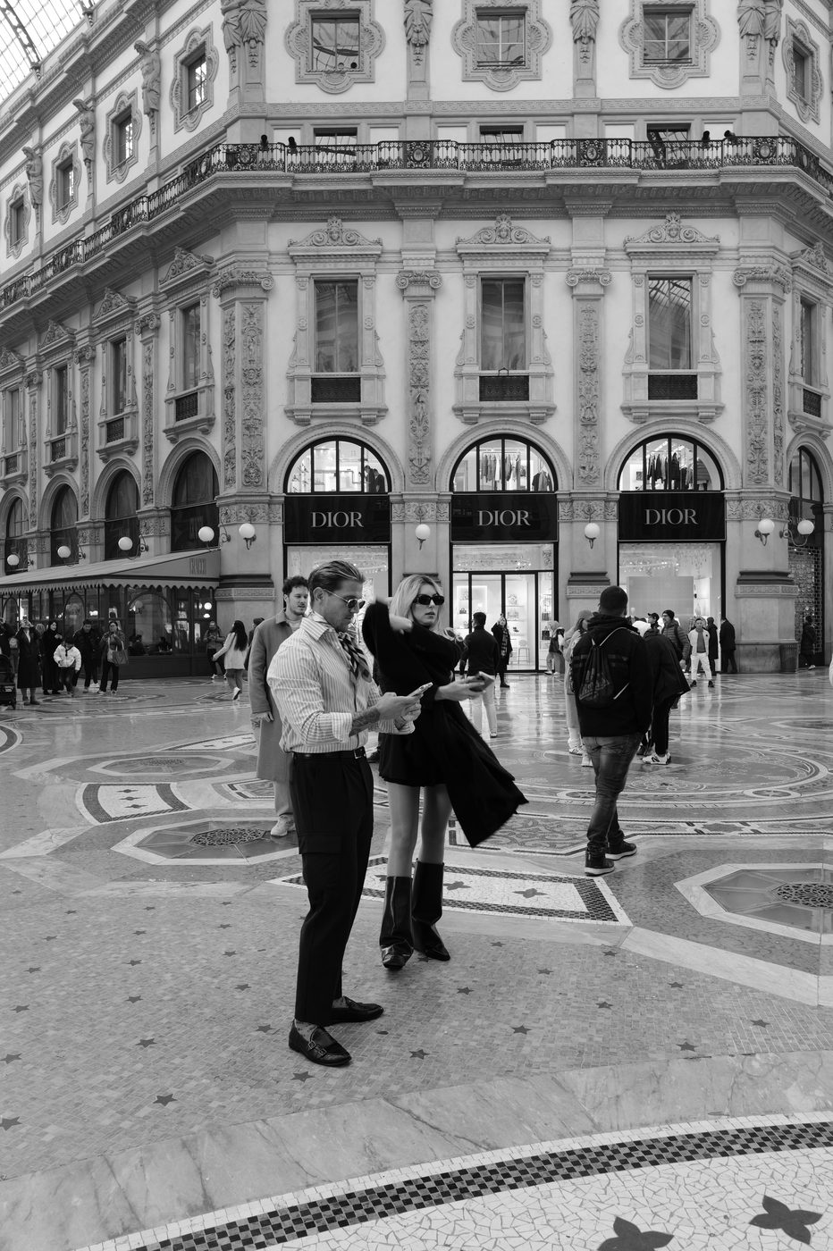 Elegant couple checking their phone in front of the Dior windows in the Galleria, Milan