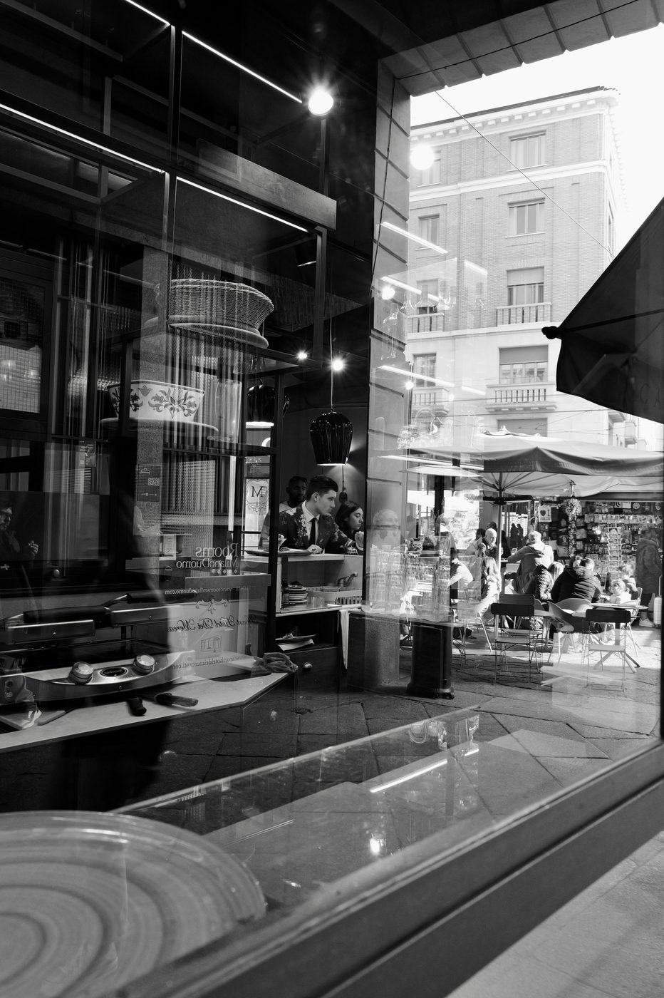 Reflection in a shop window of a lively pastry shop with its outdoor terrace, Milan