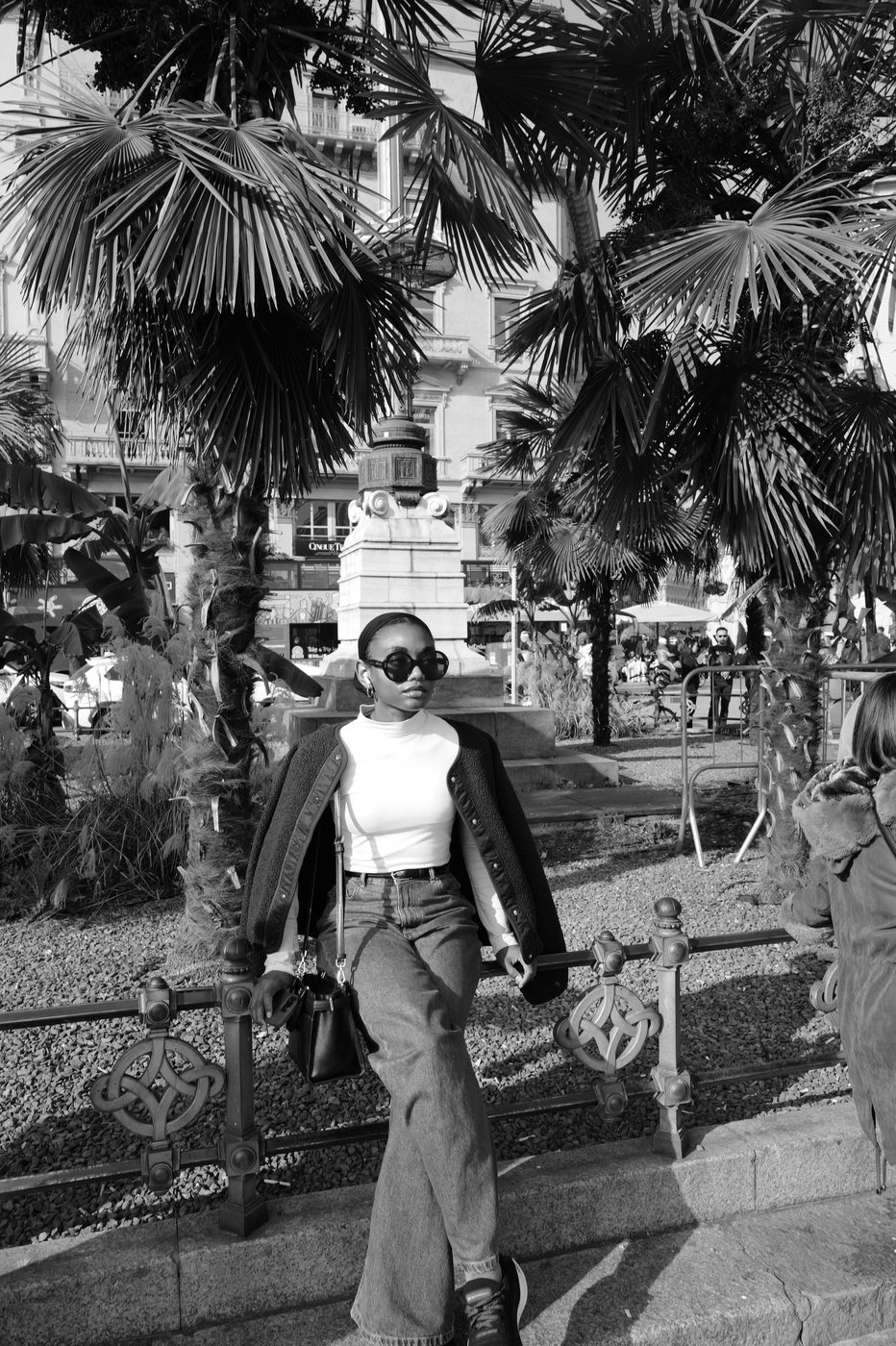 Young woman in sunglasses posing in front of palm trees near a monument, Milan