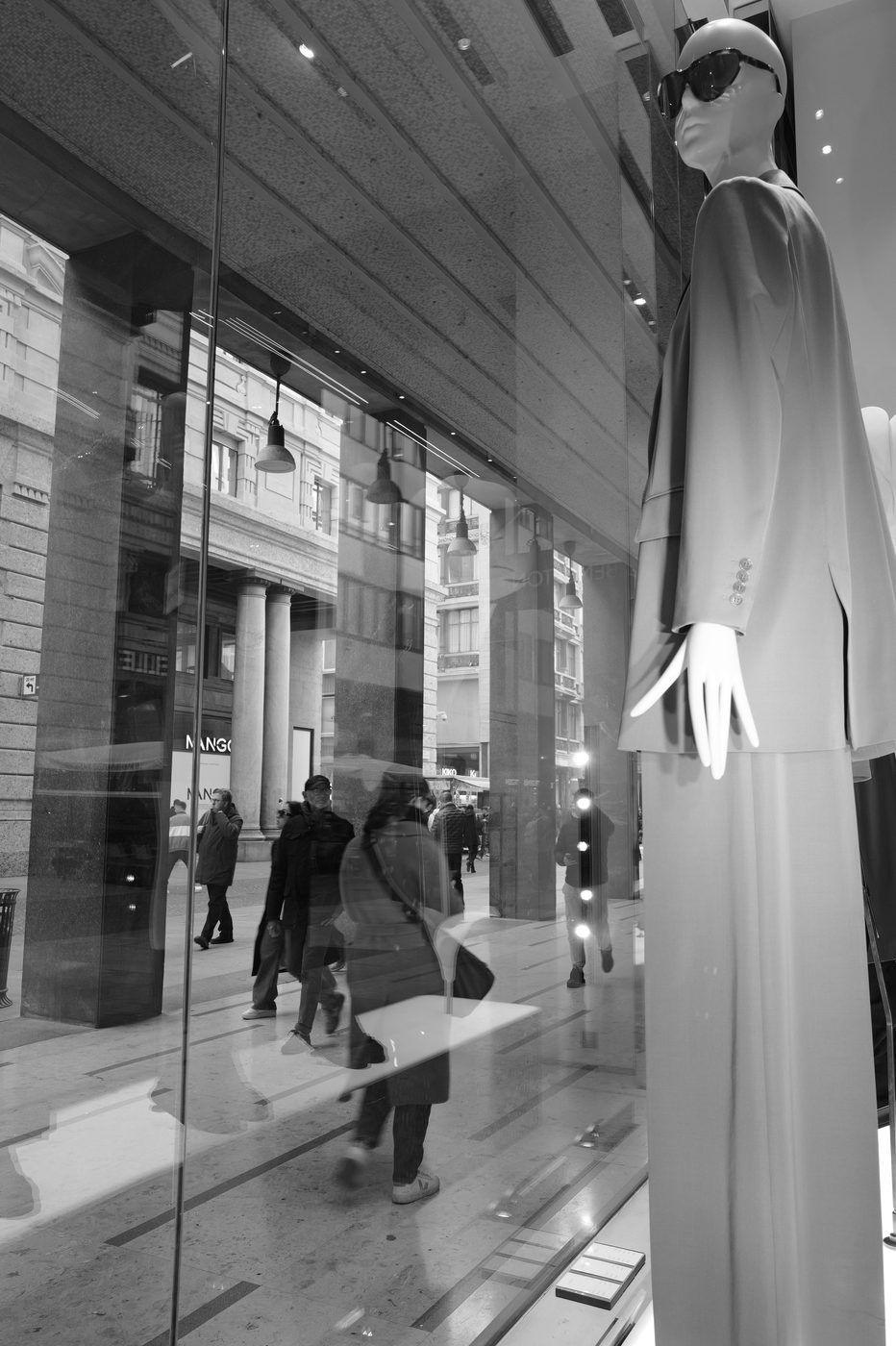 Mannequin in a shop window standing out against the blurred reflections of hurried passers-by, Milan