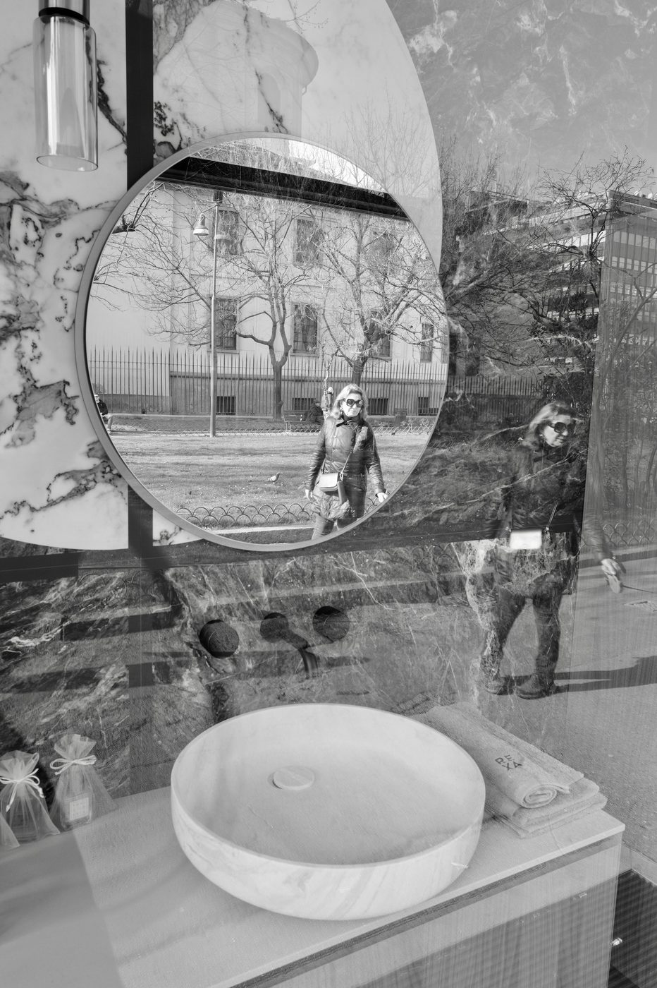 Round mirror in a shop window reflecting a passer-by in a leather jacket, Milan
