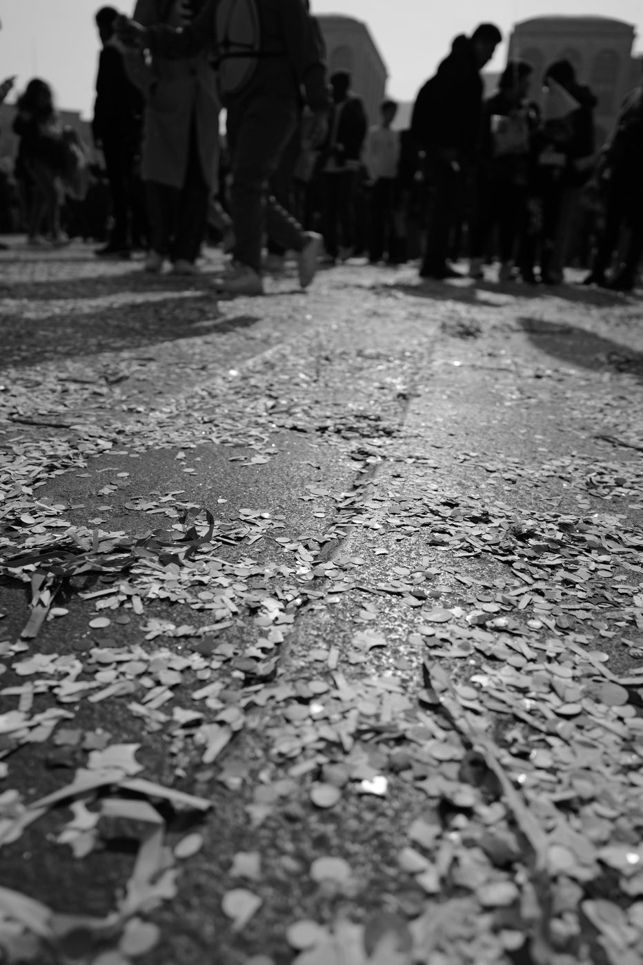 Carnival confetti scattered over the cobblestones, silhouettes of passers-by in the background, Milan