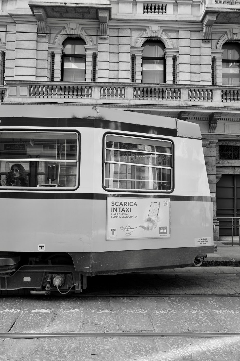 Vintage tram advertising a taxi app, passenger at the window, Milan