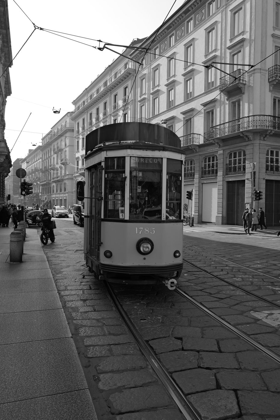 Historic tram number 1785 rolling over the cobblestones of a street lined with buildings, Milan