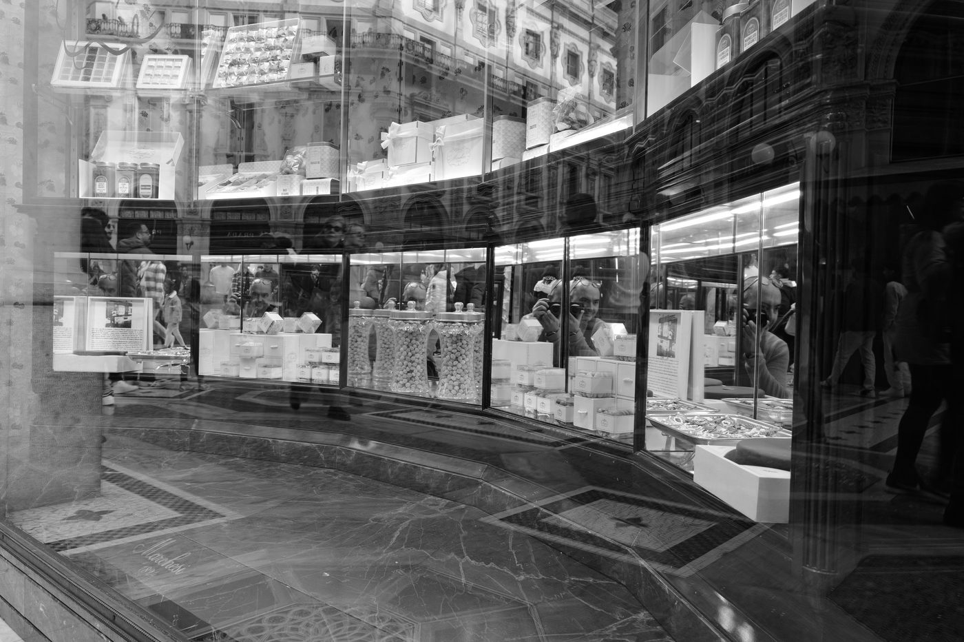 Reflection of a photographer in the curved window of a refined confectionery shop, Milan