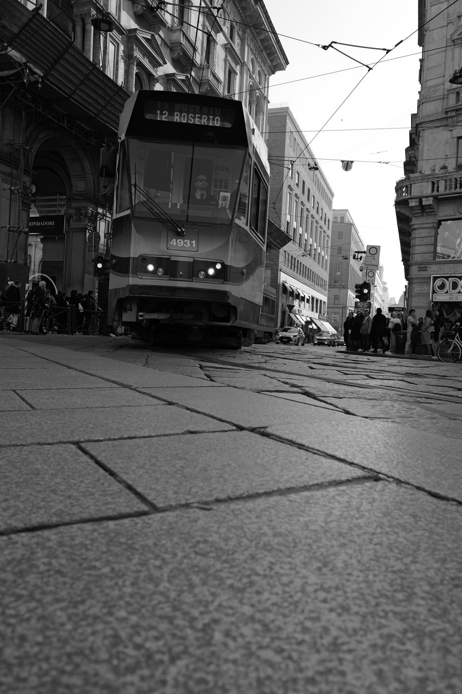 Line 12 tram approaching on the rails among the passers-by, Milan