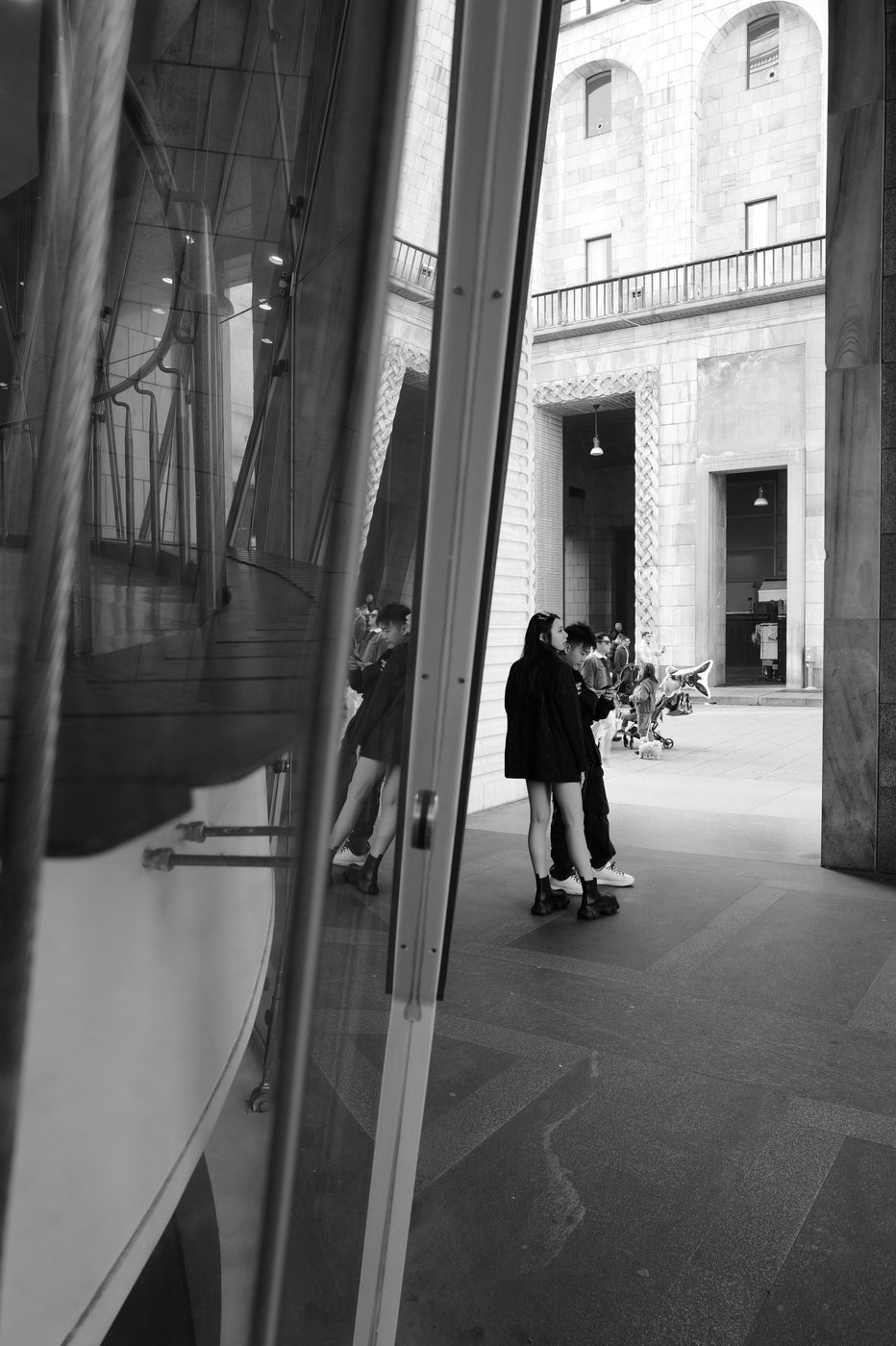 Reflection in a shop window of two young women waiting in an inner courtyard, Milan
