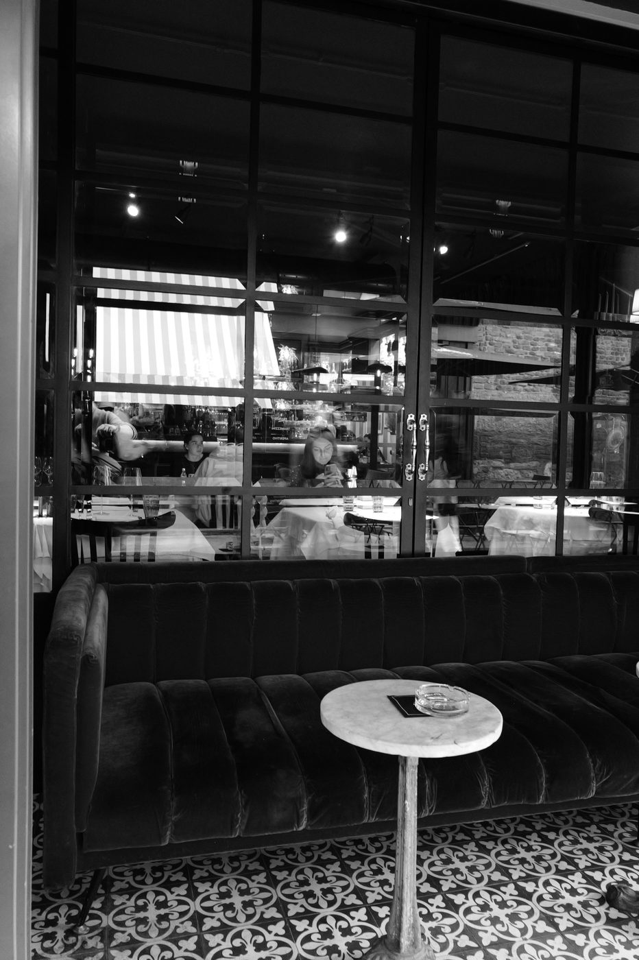 Empty velvet sofa facing a lively restaurant reflected in the window, Milan