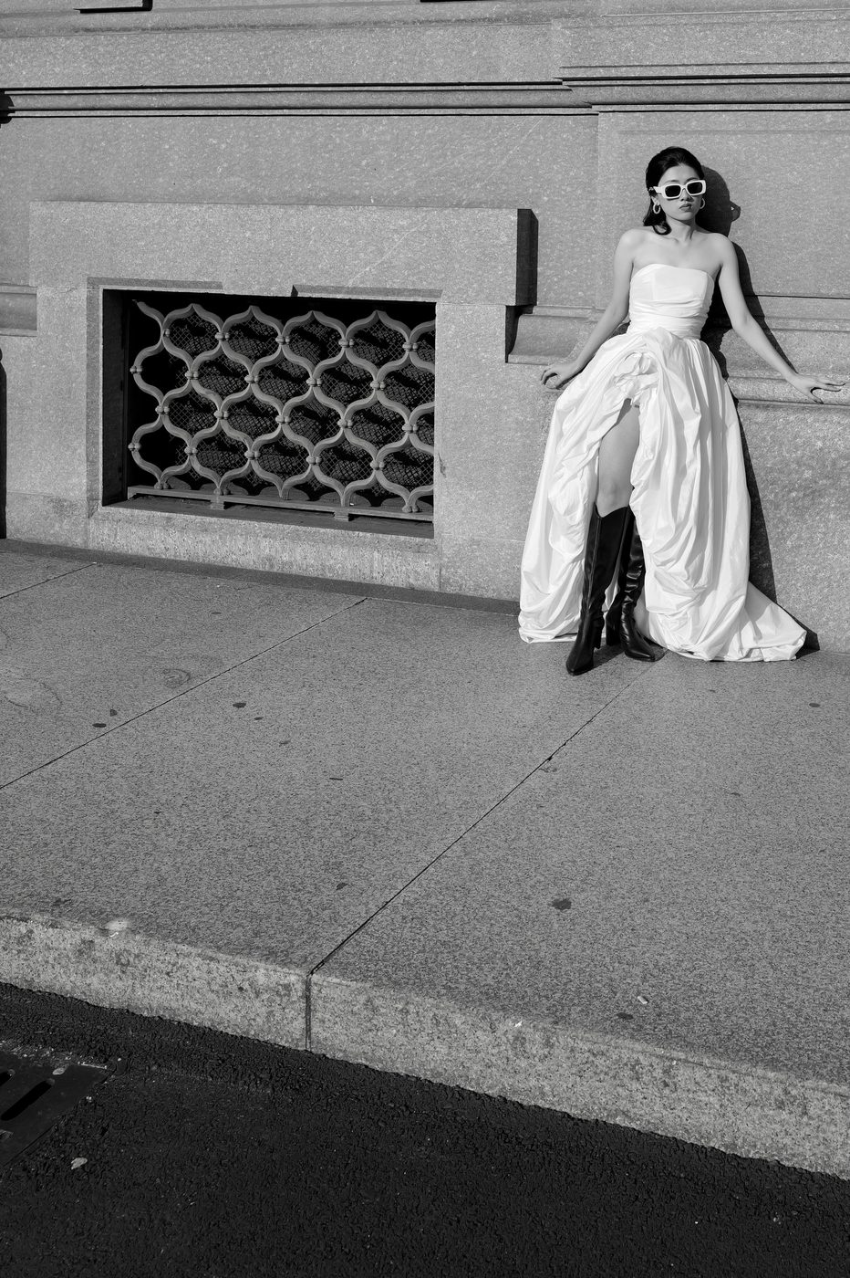 Young woman in a slit dress and tall boots posing against a stone wall, Milan