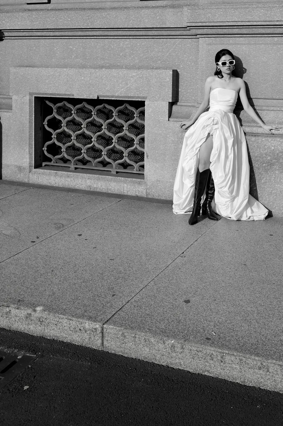Jeune femme en robe fendue et bottes hautes posant contre un mur de pierre, Milan