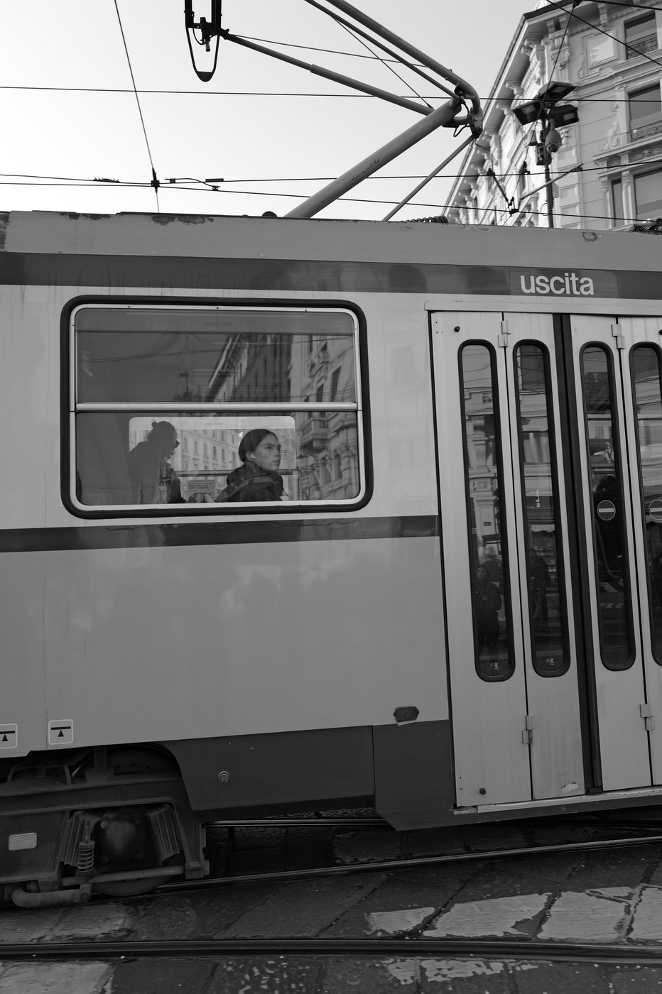 Two passengers visible through the window of a tram marked uscita, Milan
