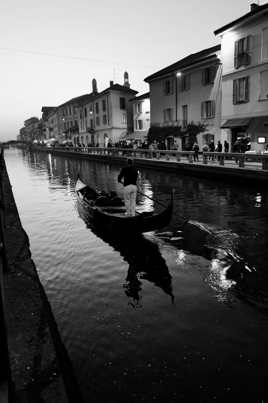 Gondolier standing and guiding his boat on the Naviglio at nightfall, Milan