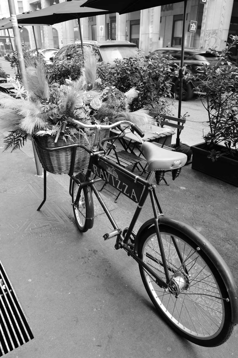 Bicycle with a basket overflowing with dried flowers parked outside a cafe terrace, Milan