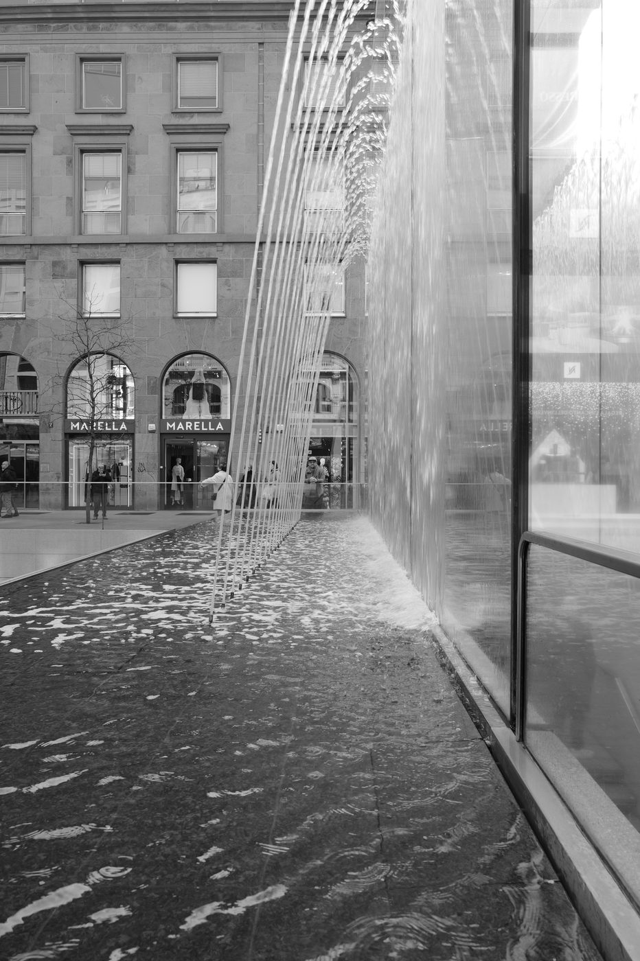 Curtain of water streaming down a glass wall in front of the Marella store, Milan