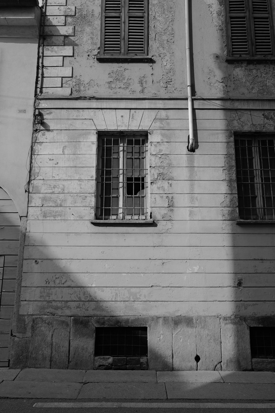 Decrepit facade with closed shutters and barred windows, raking light, Milan