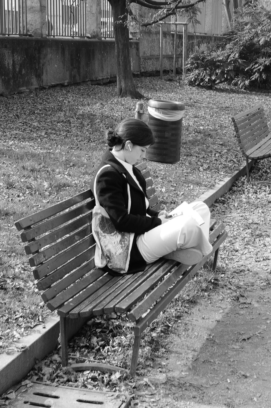 Young woman sitting cross-legged on a bench, absorbed in her reading, Milan
