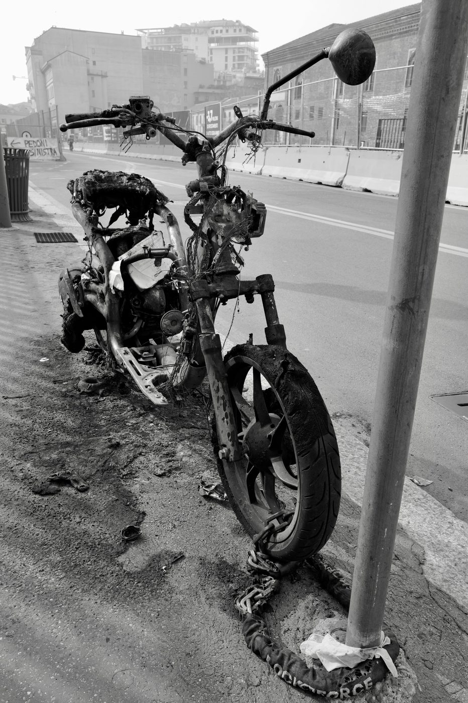 Burnt-out scooter carcass chained to a post by the roadside, Milan