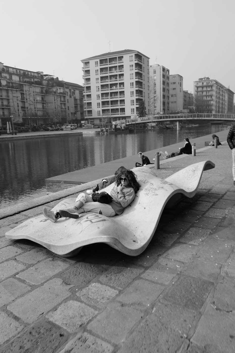 Young woman lying on a wavy concrete bench by the water, Milan
