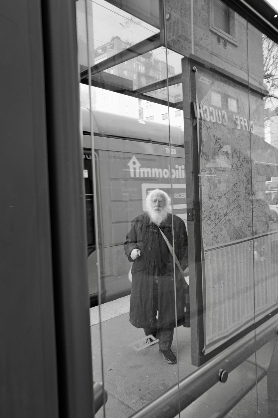 Reflection of an old bearded man at the tram stop, in front of a real estate ad, Milan