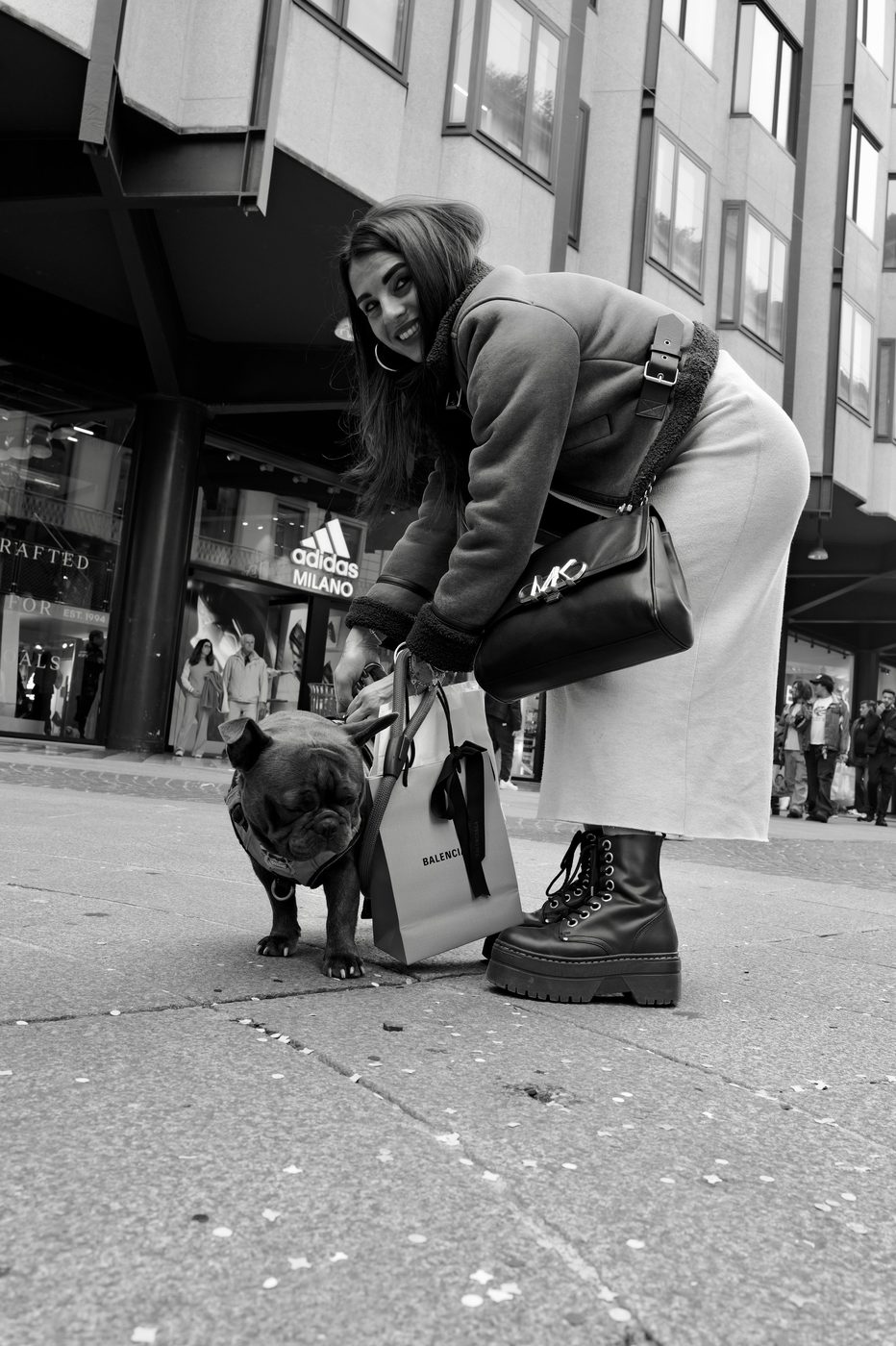 Young woman bending down to her French bulldog, Balenciaga bag in hand, Milan