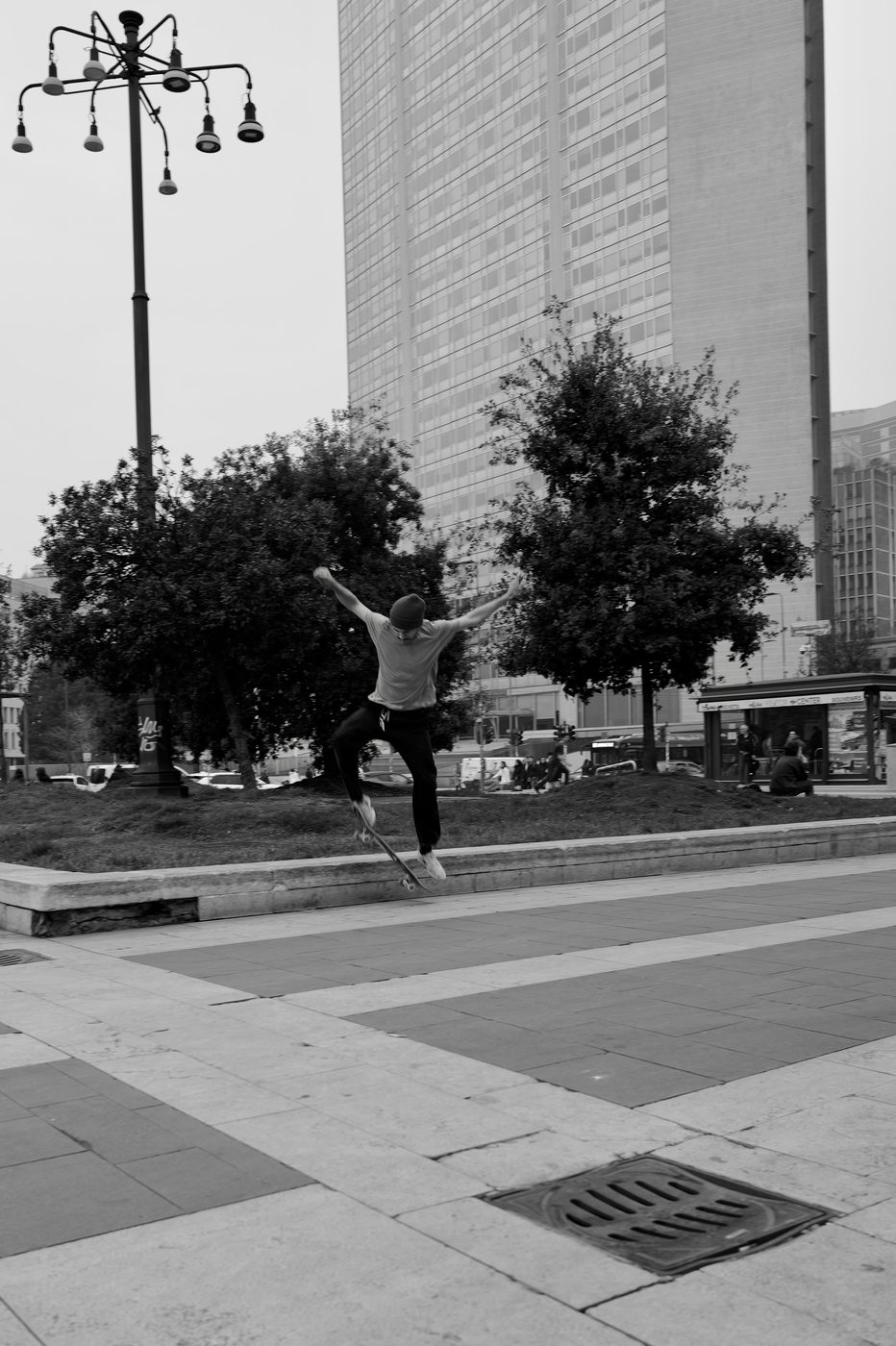 Skater mid-jump over a grate, glass tower in the background, Milan