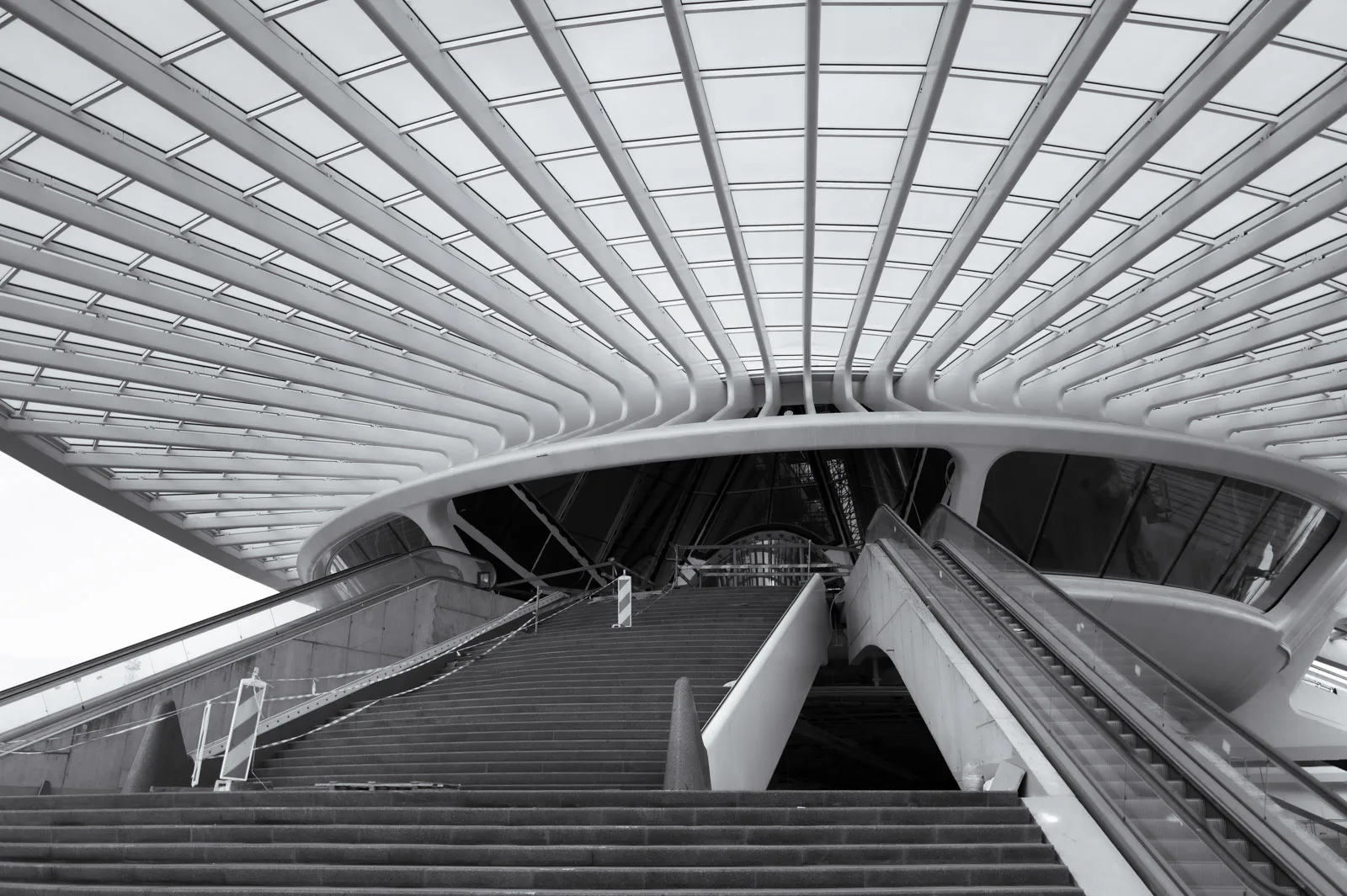 Escalier et escalator montant vers la passerelle de la gare sous ses nervures, Mons