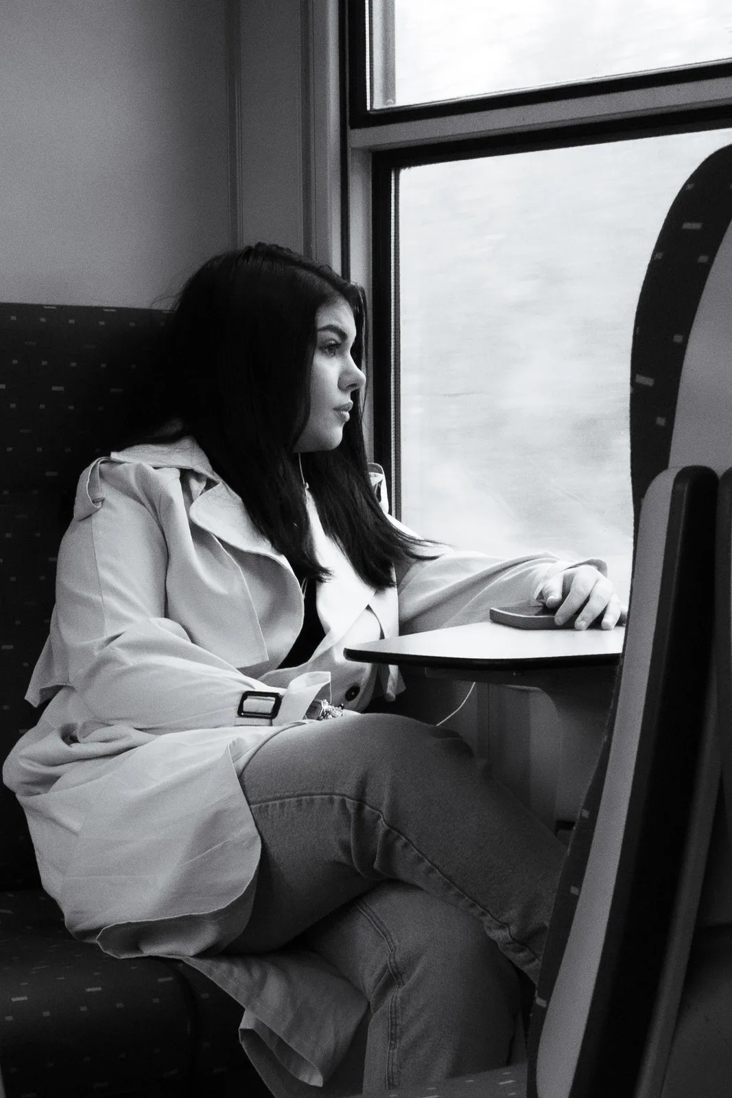 Une jeune femme en trench regarde par la fenêtre du train du retour