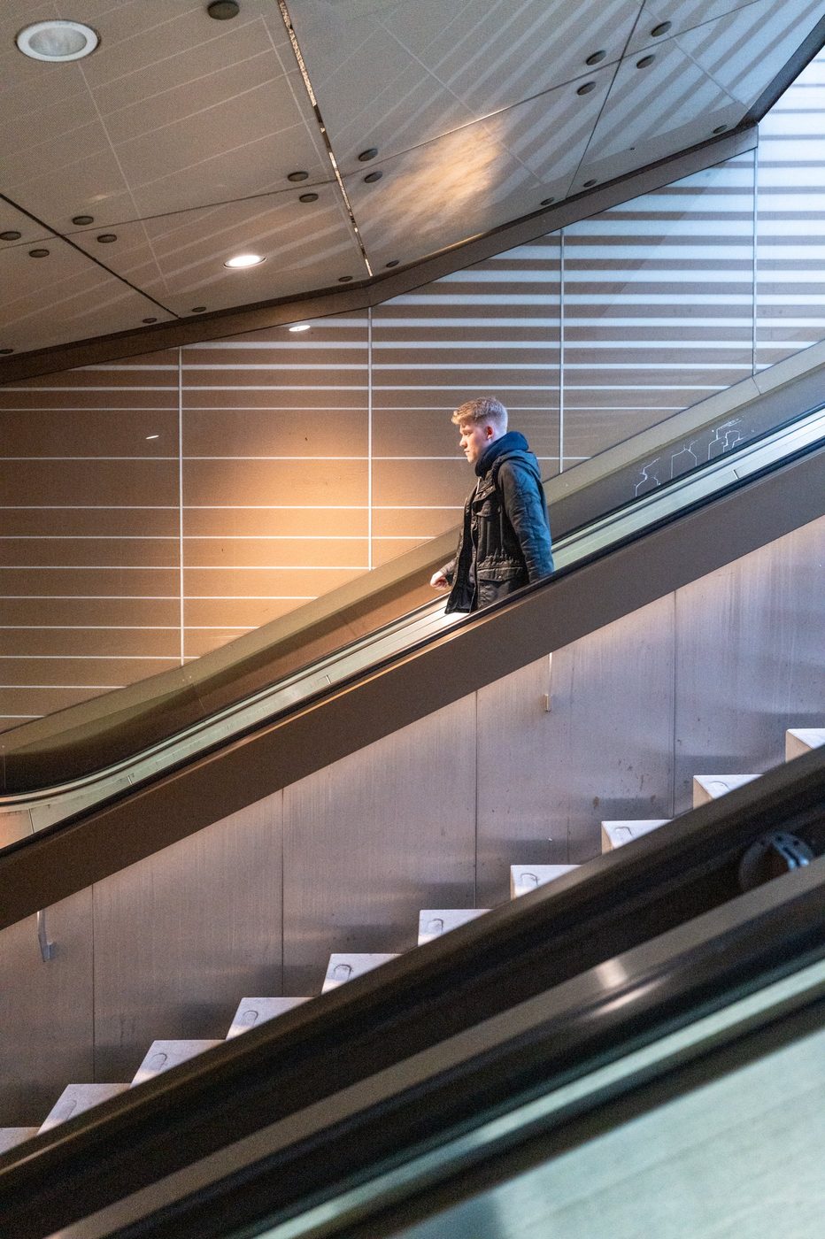 A young man goes down an escalator in a brightly lit metro station, Munich