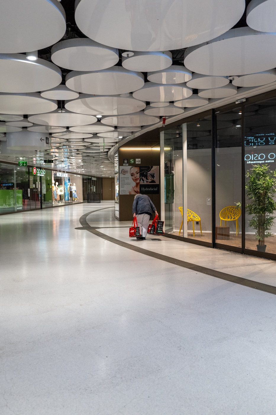 An elderly woman walks away laden with shopping bags in a shopping arcade, Munich