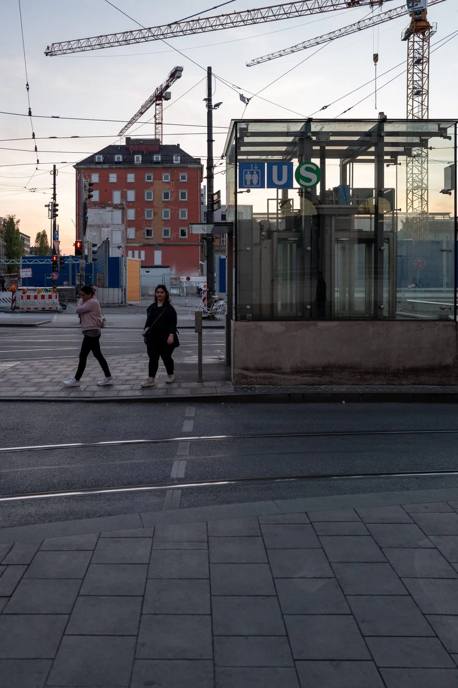 Deux passantes traversent au crépuscule près d'un accès de tramway vitré, Munich