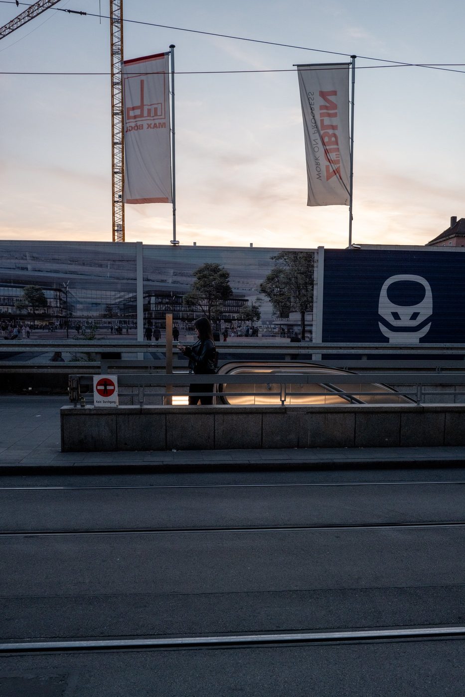 Silhouette of a woman checking her phone under advertising banners at dusk, Munich