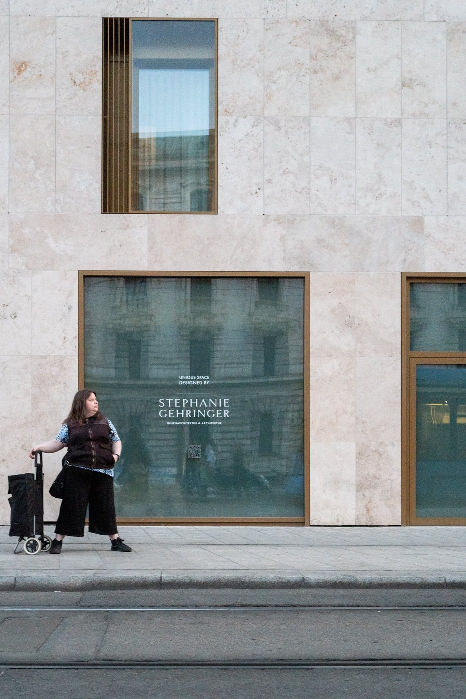 A woman pulls a shopping cart past a marble shop window, Munich