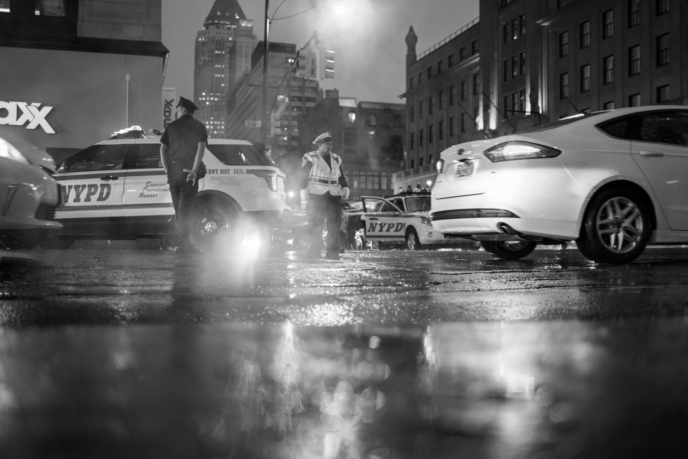Police officers by their NYPD vehicles on a wet road at night, New York