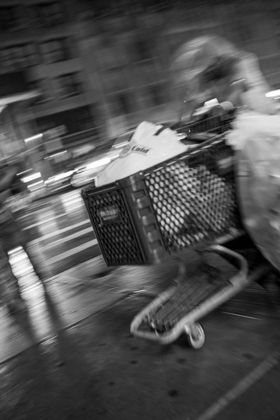 Blurred silhouette of a person pushing a loaded cart down the street at night, New York
