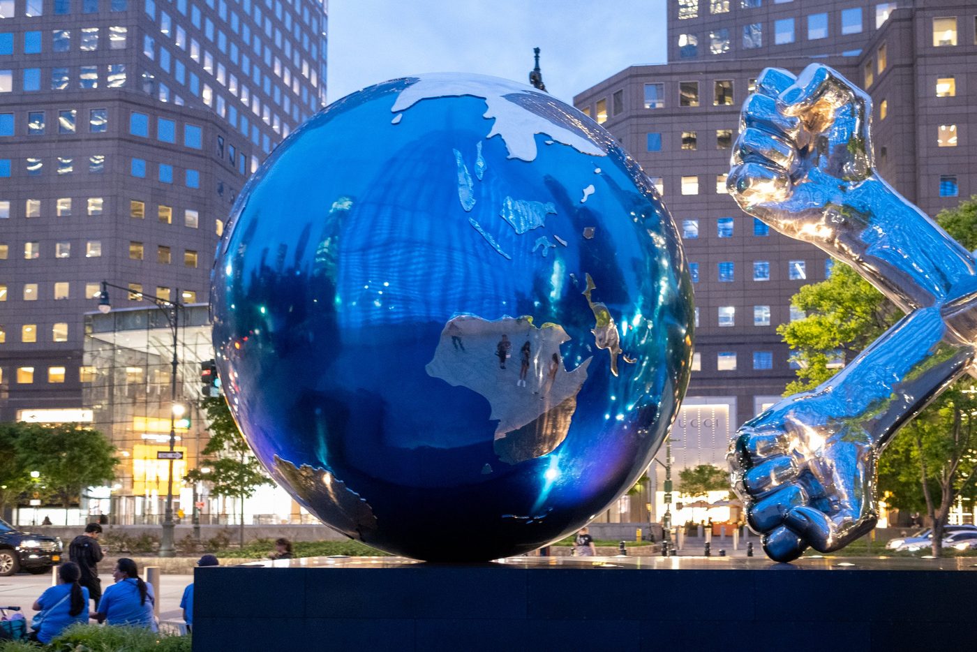 Sculpture of a metal globe and a raised fist in front of the towers at dusk, New York